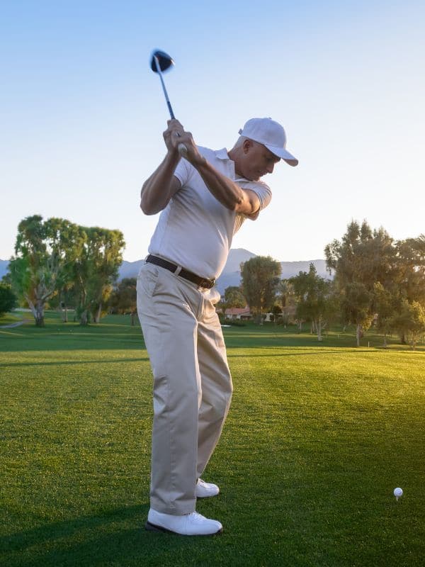Golfer holding his follow-through on the fairway at sunrise